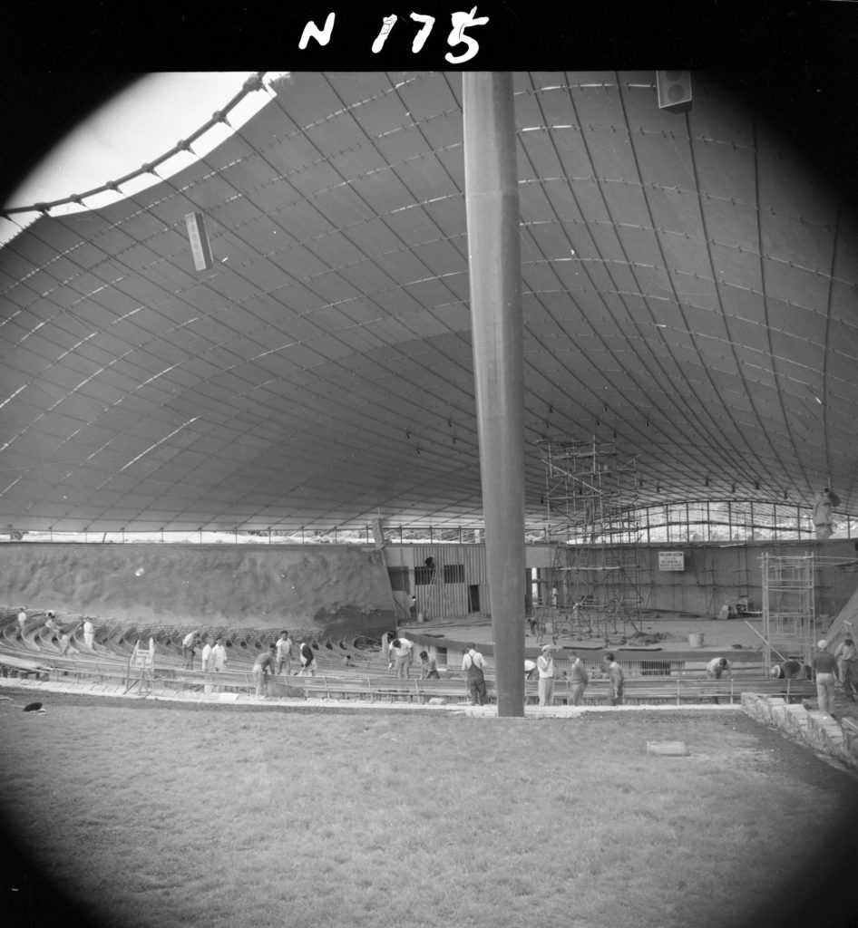 N175 Image showing carpenters and painters working on seats, and installation of stage lights during construction of the Sidney Myer Music Bowl